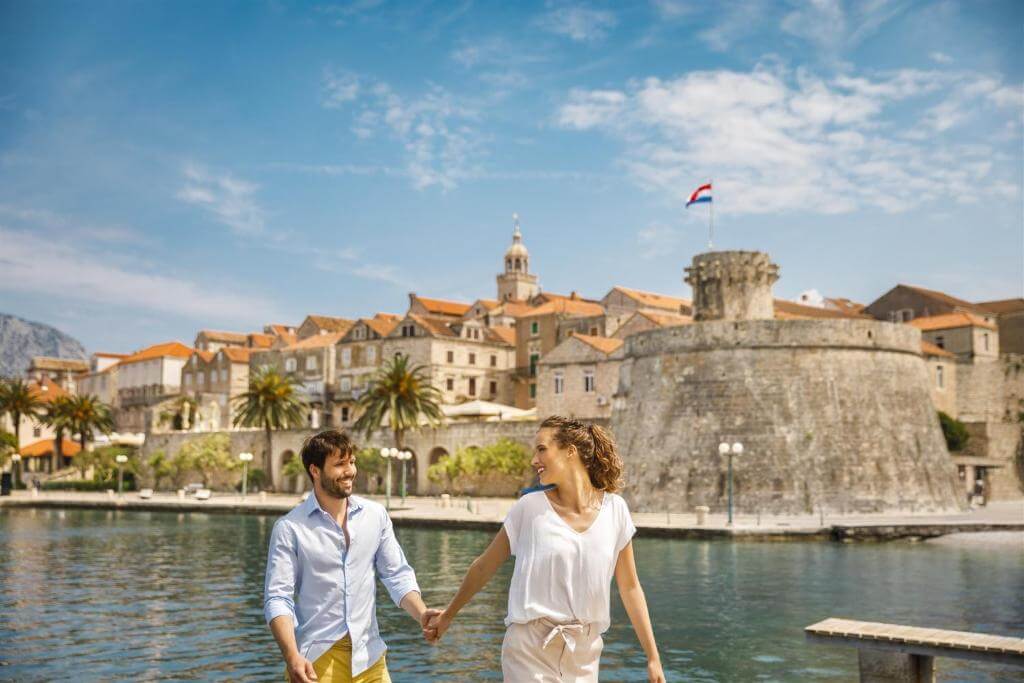 Par se drži za roke pred starim mestom na jadranski obali